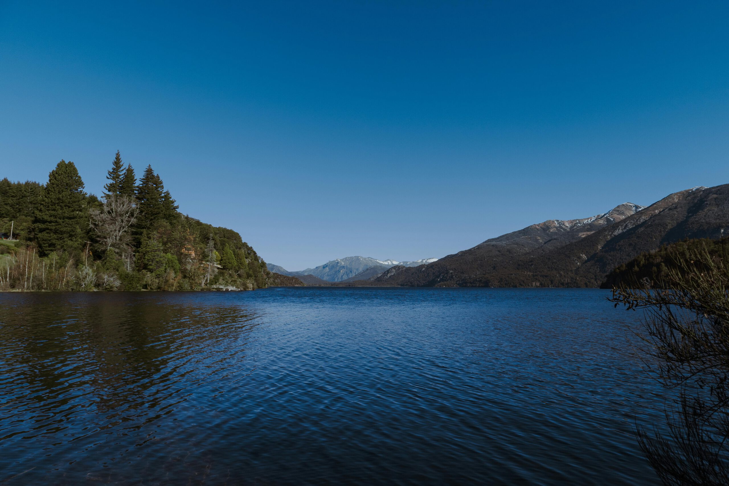 Serene lake in Bariloche, Argentina reflecting mountains under a clear sky.